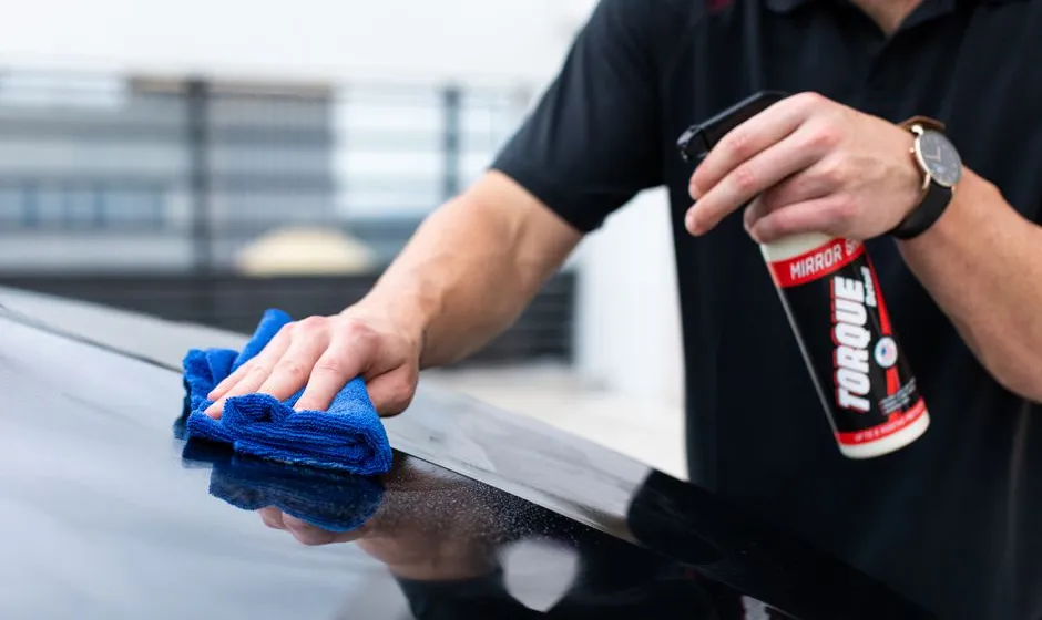 Mains gantées lavant une carrosserie bleue avec gant microfibre et mousse, gros plan